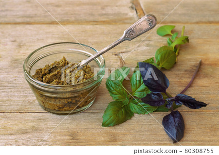Basil pesto in glass bowl with metal spoon and green purple leaves on wooden table background above 80308755