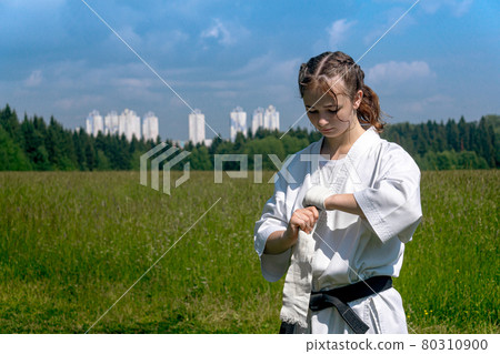 teenage girl in a kimono wrapping a wrist wrap around her hand before taking karate outdoors 80310900