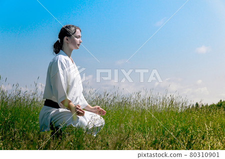 teenage girl karateka before starting training outdoor enters the mokuso meditative state in the seiza pose 80310901