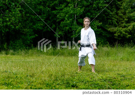 teenage girl training karate kata outdoors, performs gedan-barai (downward block) 80310904