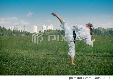 teenage girl training karate kata outdoors, performs the uro mawashi geri (hook kick) 80310905
