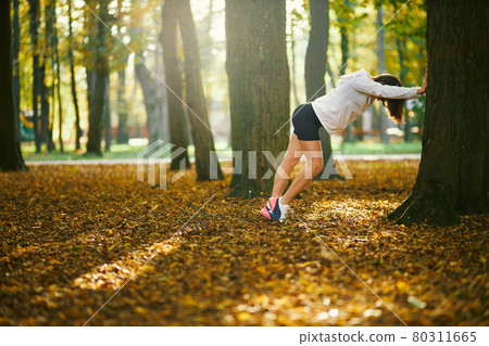 Athletic brunette stretching on the long stairs outdoors, looking