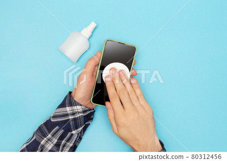 A man in a shirt disinfects his phone and wipes it with a cotton pad treated with an antiseptic. Coronavirus protection. A man in a shirt disinfects his phone and wipes it with a cotton pad treated with an antiseptic. Coronavirus protection. 80312456