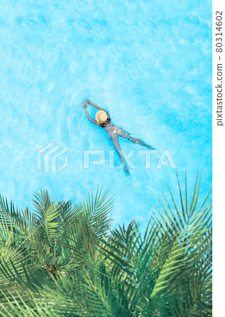 Top view of young woman in bikini and straw hat is swimming in transparent blue sea, lagoon under palm trees. Aerial, drone view Top view of young woman in bikini and straw hat is swimming in transparent blue sea, lagoon under palm trees. Aerial, drone view 80314602