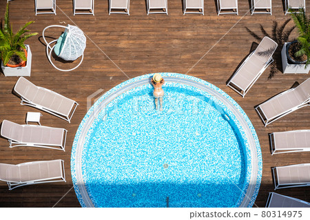 Young alone beautiful sports woman in bikini and hat is swimming in jacuzzi on wooden terrace. Aerial drone view from above. Tropical summer luxury hotel Young alone beautiful sports woman in bikini and hat is swimming in jacuzzi on wooden terrace. Aerial drone view from above. Tropical summer luxury hotel 80314975