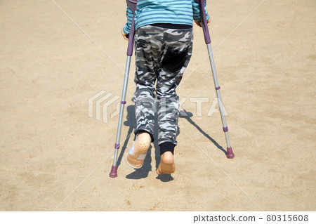 A little boy with Autism, Asperger syndrome on crutches after breaking his leg walks on the beach. 80315608