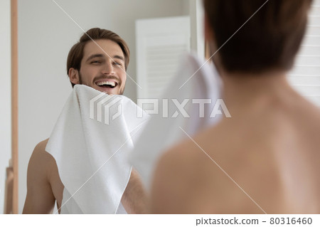 Happy attractive young millennial guy drying beard with white towel Happy attractive young millennial guy drying beard with white towel 80316460