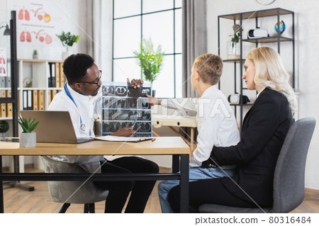 African pediatrician explaining tomography scan to his teen boy-patient and caring mother African pediatrician explaining tomography scan to his teen boy-patient and caring mother 80316484