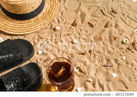 Summer beachwear, flip flops, hat, cold drink in a glass and seashells on sand beach. 80317094