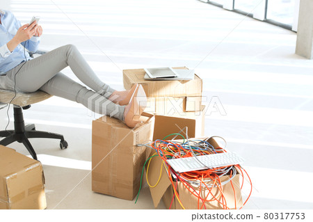 Low section of businesswoman holding mobile phone with feet up on cardboard box at office Low section of businesswoman holding mobile phone with feet up on cardboard box at office 80317753