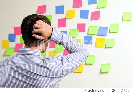 Businessman looking at wall of sticky notes with hands behind head 80317792