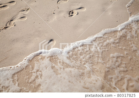 Footprints of bare feet are over a wet sand on the beach 80317825