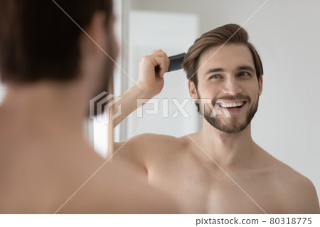 Happy handsome young shirtless man combing smooth straight hair 80318775