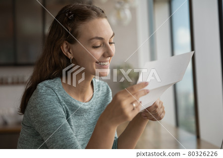 Smiling young woman reading paper correspondence letter. Smiling young woman reading paper correspondence letter. 80326226