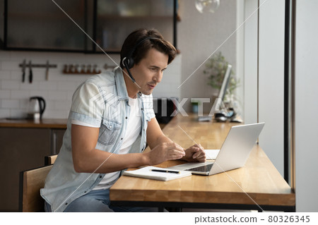 Focused young man in wireless headset holding video call. Focused young man in wireless headset holding video call. 80326345