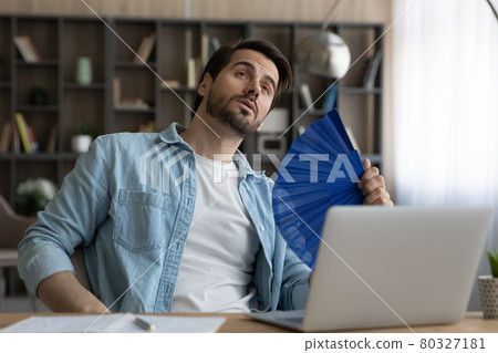 Unhappy overheated young male worker using paper fan. 80327181