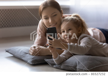 Elder sister rest on pillows with younger one use cellphone 80327232