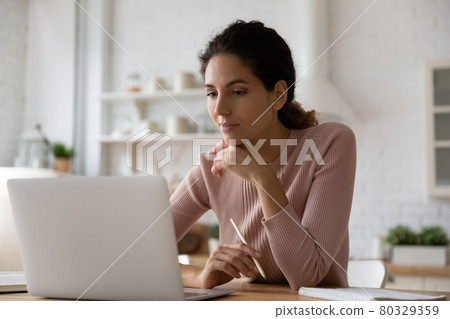 Focused young beautiful woman using computer in modern kitchen. 80329359