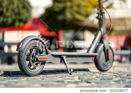 Electric scooter parked on tiled cobblestone pavement - closeup detail on rear wheel with disc brake 80329677
