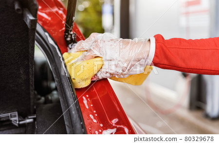 Young woman cleaning rear part of her car, closeup detail on hand in glove holding yellow sponge 80329678