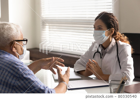 Female doctor and old patient wear facemasks in consultation Female doctor and old patient wear facemasks in consultation 80330540
