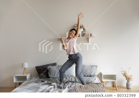 Happy young hispanic woman dancing on bed. 80332399