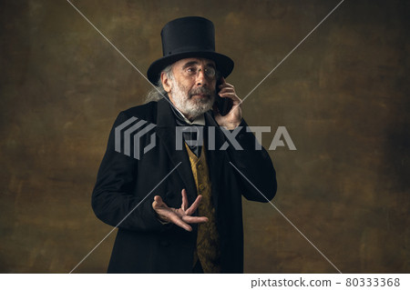 Cute senior man, gentleman, aristocrat or actor talking on phone isolated on dark vintage background. Retro style, comparison of eras concept. 80333368