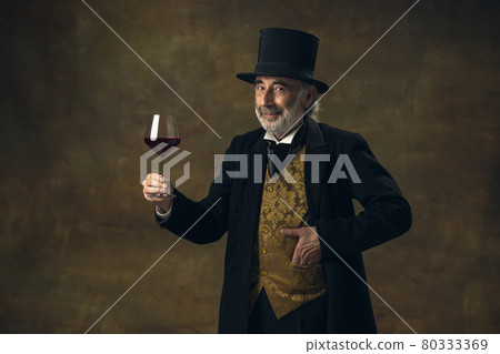 Portrait of elderly gray-haired man, gentleman, aristocrat or actor tasting wine isolated on dark vintage background. Retro style, comparison of eras concept. 80333369