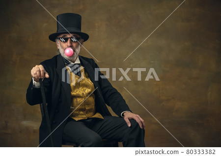 Cute senior smiling man, gentleman, aristocrat or actor watching movie isolated on dark vintage background. Retro style, comparison of eras concept. Cute senior smiling man, gentleman, aristocrat or actor watching movie isolated on dark vintage background. Retro style, comparison of eras concept. 80333382