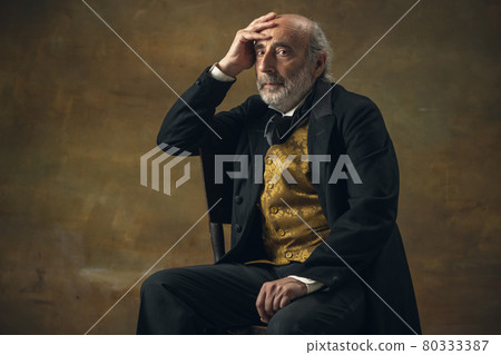 Half-length retro portrait of sad elderly gray-haired man, gentleman, aristocrat or actor isolated on dark vintage background. Retro style, comparison of eras concept. Half-length retro portrait of sad elderly gray-haired man, gentleman, aristocrat or actor isolated on dark vintage background. Retro style, comparison of eras concept. 80333387