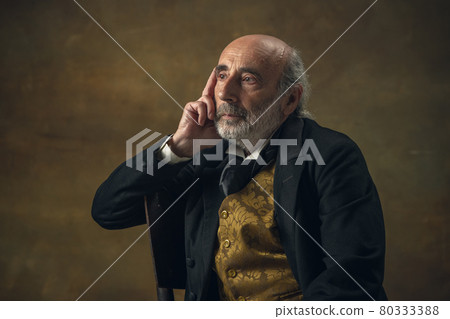 Half-length retro portrait of sad elderly gray-haired man, gentleman, aristocrat or actor isolated on dark vintage background. Retro style, comparison of eras concept. Half-length retro portrait of sad elderly gray-haired man, gentleman, aristocrat or actor isolated on dark vintage background. Retro style, comparison of eras concept. 80333388