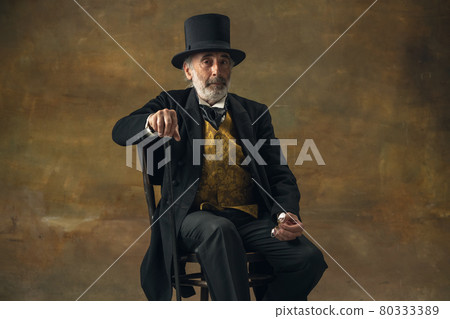 Half-length retro portrait of sad elderly gray-haired man, gentleman, aristocrat or actor isolated on dark vintage background. Retro style, comparison of eras concept. Half-length retro portrait of sad elderly gray-haired man, gentleman, aristocrat or actor isolated on dark vintage background. Retro style, comparison of eras concept. 80333389