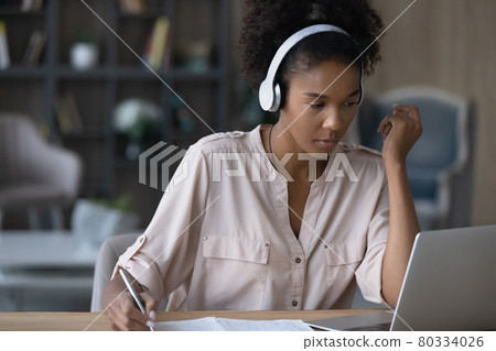 Close up focused African American woman in headphones taking notes 80334026
