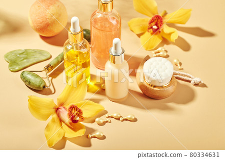 Cosmetic care products in glass bottles with orchid flowers - serums, cream, gel, oils. Concept for face and body care, wellness and spa, tropical relaxation. 80334631