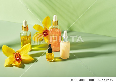 Cosmetic care products in glass bottles with orchid flowers - serums, cream, gel, oils. Concept for face and body care, wellness and spa, tropical relaxation. 80334659