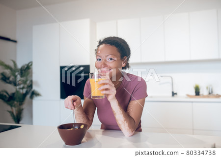 Young dark-skinned woman holding a glass with orange juice Young dark-skinned woman holding a glass with orange juice 80334738