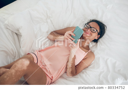 Young smiling woman lying in bed and texting 80334752