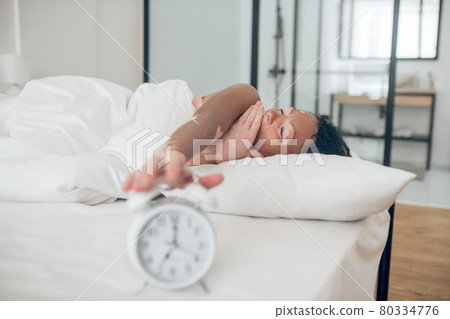 Young dark-skinned woman lying in bed and switching the alarm off 80334776