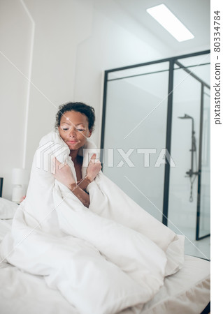 Young woman sitting in bed covered with blanket and feeling relaxed Young woman sitting in bed covered with blanket and feeling relaxed 80334784