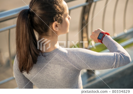 Waist up picture of a long-haired girl looking at her smartwatch 80334829