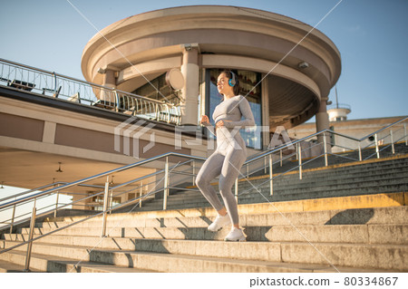 Fit girl in grey sportswear having cardio warm up on the stairs 80334867