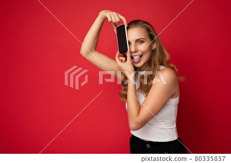 Shot of pretty funny young blonde female person wearing white t-shirt isolated on red background 80335837