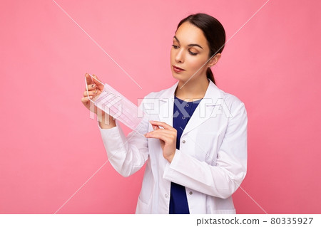 Beautiful young woman holds and wears a white medical mask to protect yourself from corona virus 80335927