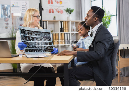 Woman doctor holding x-ray scan, talking with black-skinned father with cute mixed race daughter Woman doctor holding x-ray scan, talking with black-skinned father with cute mixed race daughter 80336166