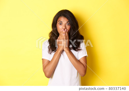 Portrait of startled african-american woman, gasping and covering mouth with hands, looking shocked at camera, standing over yellow background for copy space Portrait of startled african-american woman, gasping and covering mouth with hands, looking shocked at camera, standing over yellow background for copy space 80337140