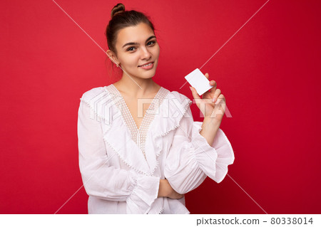 Beautiful happy young dark blonde woman wearing white blouse isolated over red background holding Beautiful happy young dark blonde woman wearing white blouse isolated over red background holding 80338014