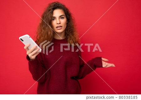 Photo of pretty asking upset young woman with curly hair wearing dark red sweater isolated on red 80338185