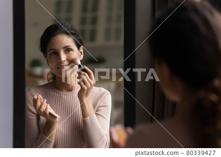 Happy attractive young woman applying powder rosy blushes. Happy attractive young woman applying powder rosy blushes. 80339427