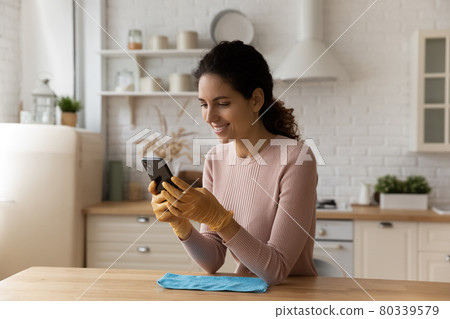 Distracted from cleaning young woman sending message on smartphone. Distracted from cleaning young woman sending message on smartphone. 80339579