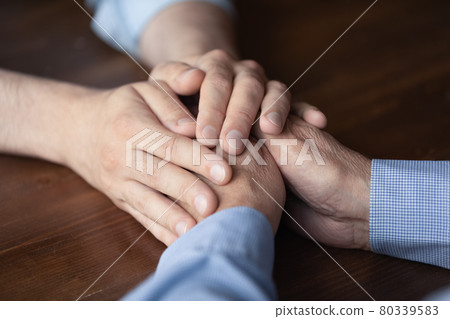 Young man holding hands of elderly father close up Young man holding hands of elderly father close up 80339583